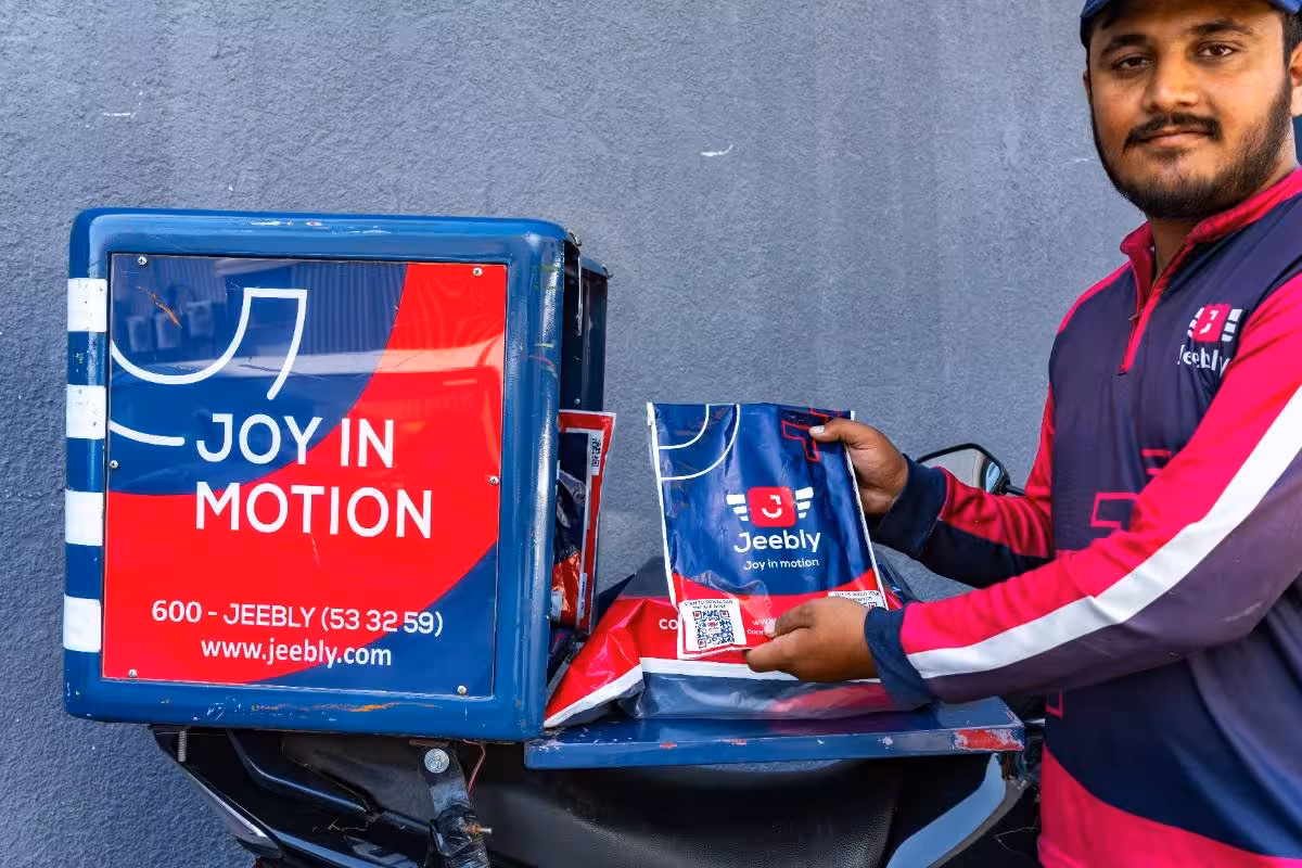 Jeebly delivery rider holding a package next to a branded motorcycle box in the UAE